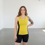 Pivotstar yellow athletic tank top with black side panels, racerback, and logo detail. Model wears black shorts.